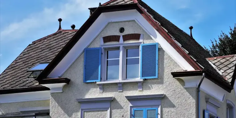 Exterior view of a suburban house with a steep roof and blue window shutters, illustrating attic ventilation context