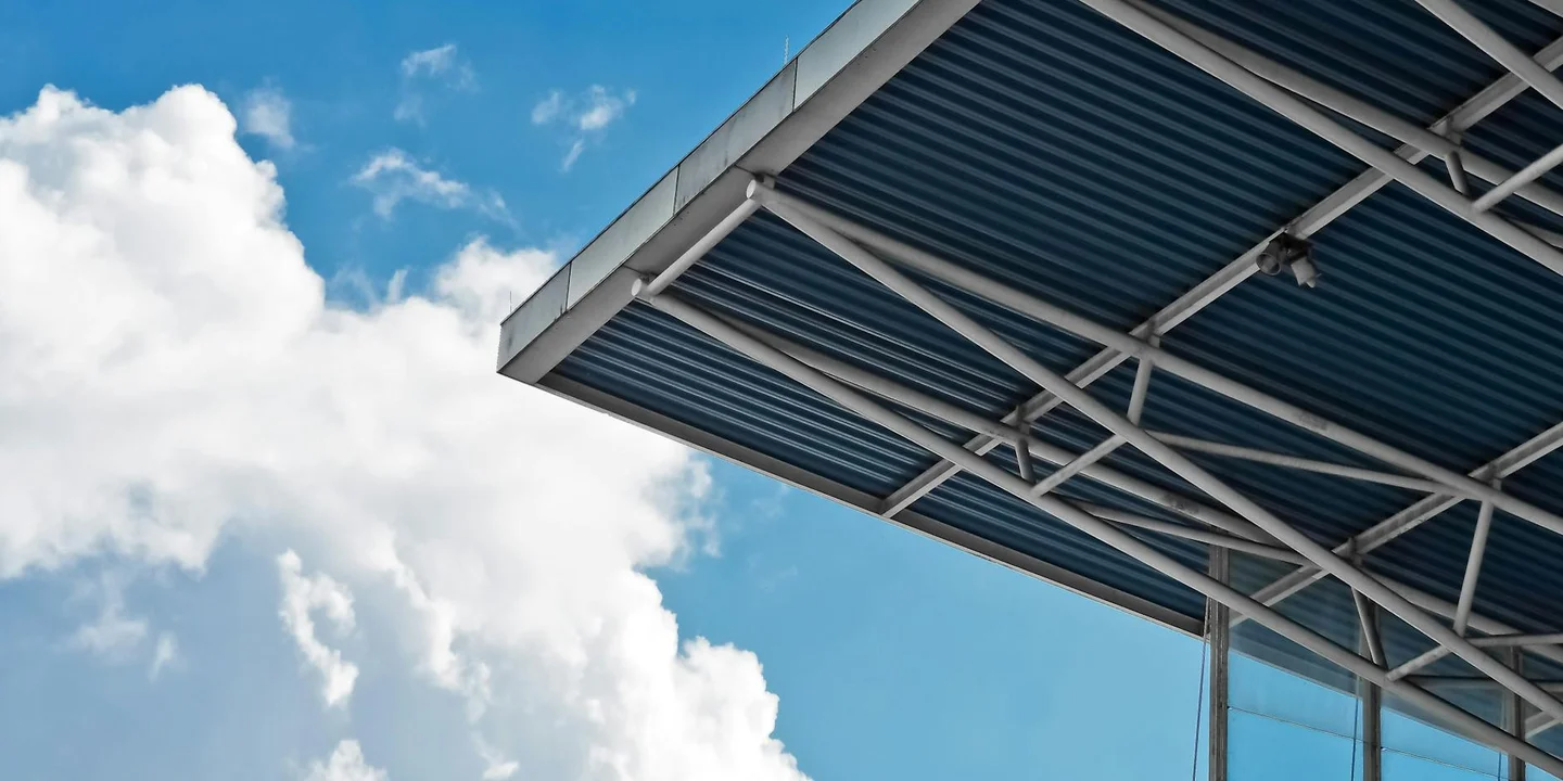 Close-up of a metal roof canopy with exposed steel framing against a bright blue sky.