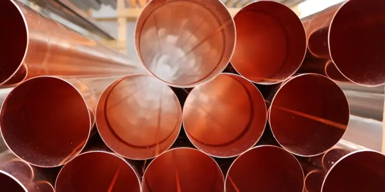 Close-up of stacked red-orange cylindrical metal pipes with circular openings.
