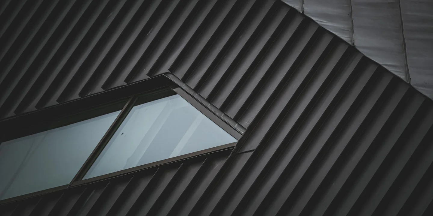 Close-up view of dark ribbed metal roofing panels with a small skylight window.