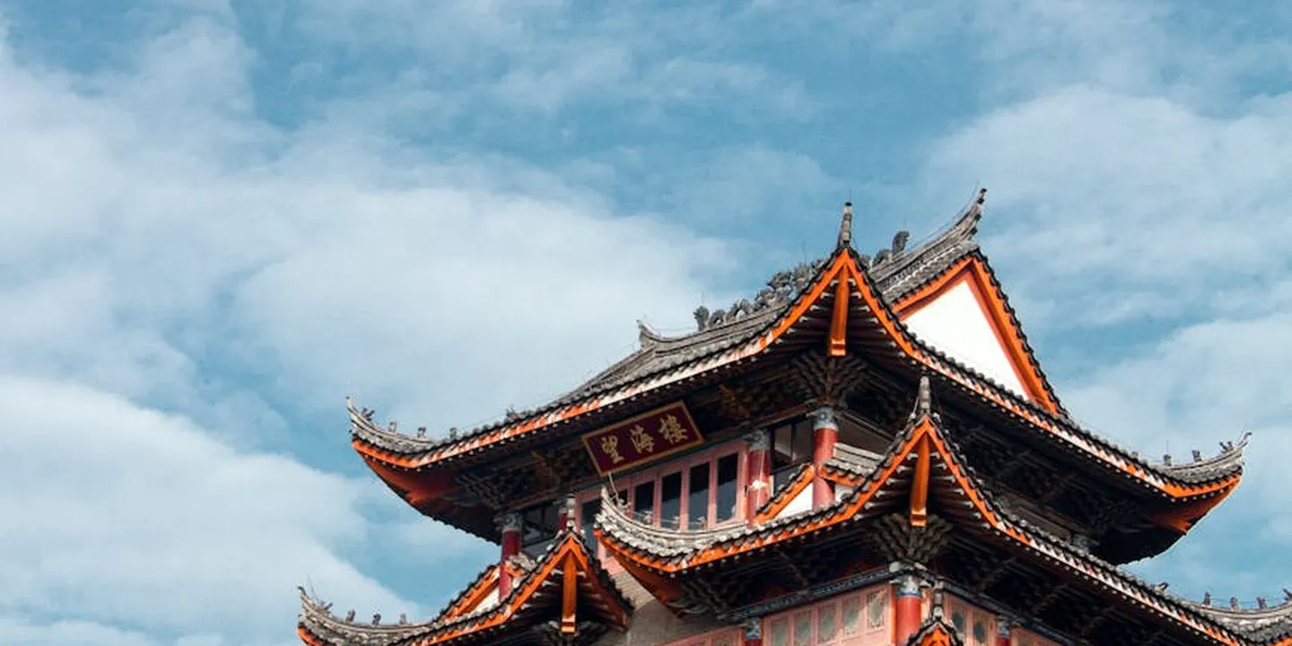 A multi-tier traditional pagoda roof with ornate wooden eaves and exposed beams against a blue sky