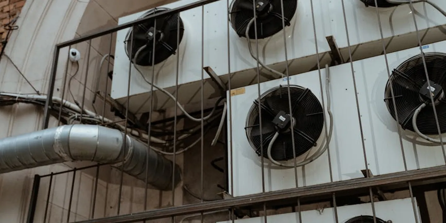Exterior wall with multiple round vent fans and attached ductwork, part of an HVAC system on a building’s roof edge.