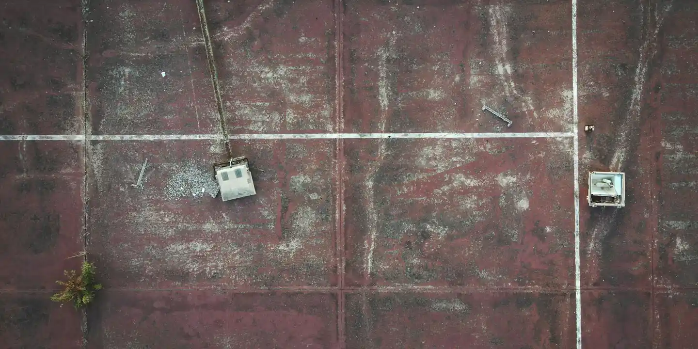 Top-down view of a weathered flat roof with a reddish surface, white grid lines, and small square vent fixtures.