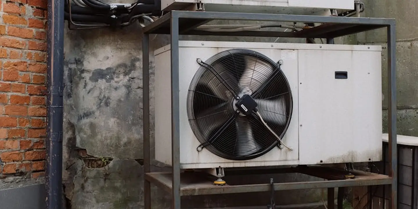 Outdoor HVAC condenser unit mounted on a metal frame beside a brick wall, illustrating exterior building components near the roofline.