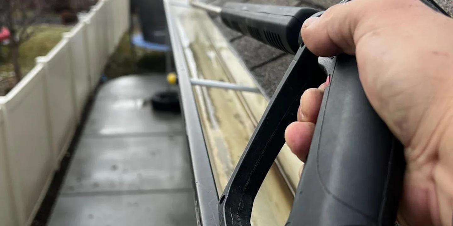 Close-up of a hand using a drill to secure a gutter bracket along the roof edge to address sagging gutters.