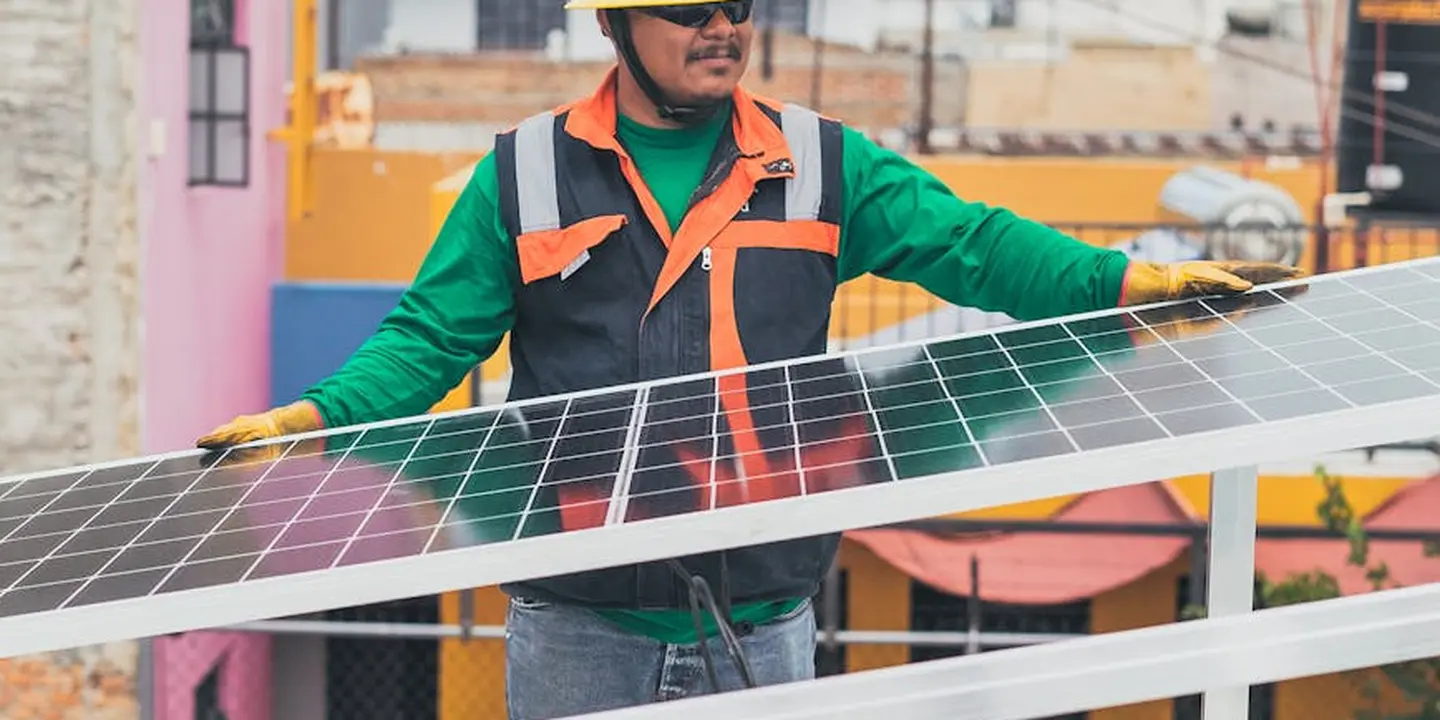 Rooftop solar installer in safety gear handling a solar panel.