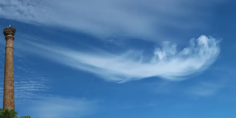 Brick chimney against a bright blue sky with wispy white clouds
